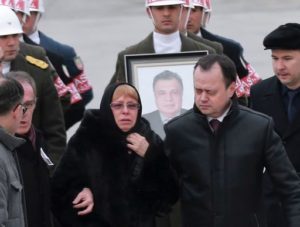Marina Davydova Karlova,  (C) widow of Russian Ambassador to Turkey Andrei Karlov, stands in front of a picture of her late husband during a ceremonial farewell with full state honours on the tarmac of Ankara's Esenboga Airport in Ankara on December 20, 2016, before the coffin is transported on a Russian plane for Moscow. Veteran diplomat Andrei Karlov was shot nine times in the back by an off-duty Turkish policeman at the opening of an exhibition of Russian photography on December 19, 2016. The brazen killing stunned Ankara and Moscow, which have rowed repeatedly over the Syria conflict but in recent weeks have begun cooperating closely on the evacuations from war-wrecked Aleppo. / AFP PHOTO / ADEM ALTAN